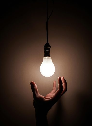 A hand reaching towards a glowing hanging light bulb symbolizing creativity and illumination.